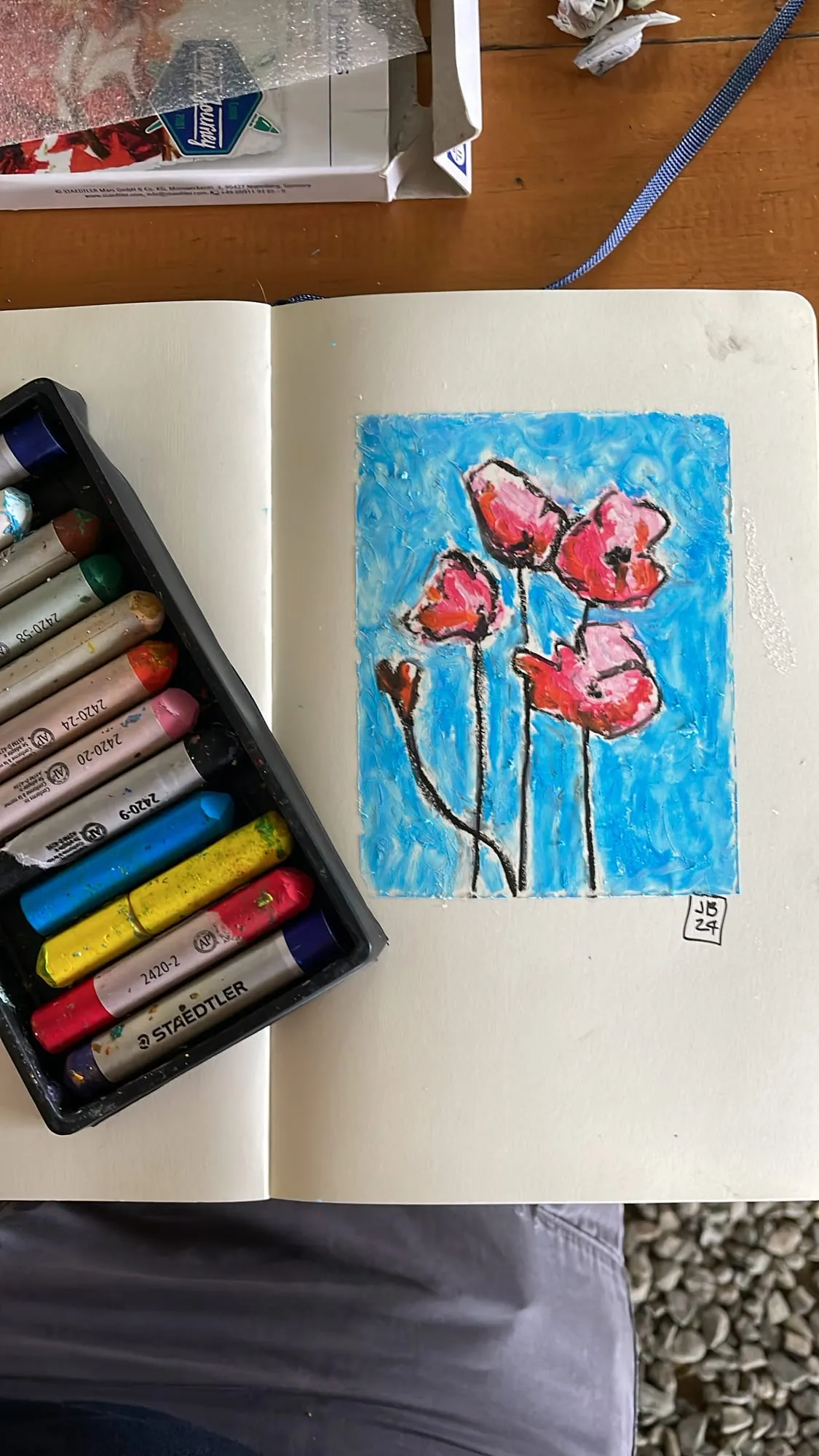 Amapolas — flores rojas sobre fondo azul en óleo pastel, junto a la caja de pasteles
